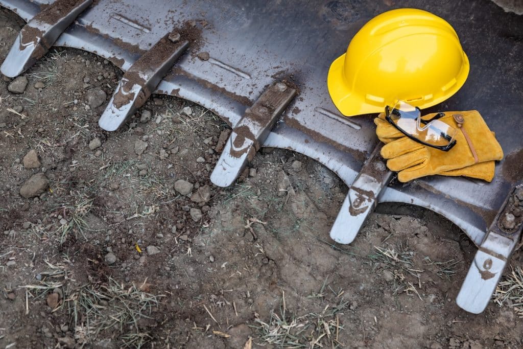Hardhat, work gloves, and safety glasses resting on the ground at a job site